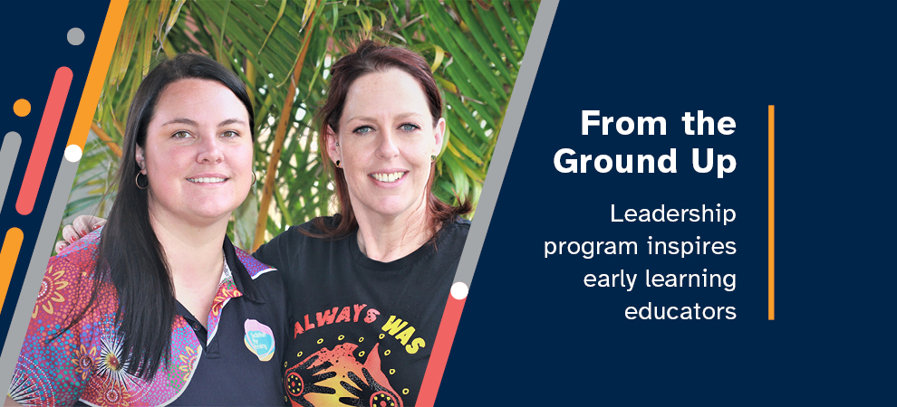 Two child care workers smiling and wearing colourful indigenous Australian t-shirts, with green, leafy plants in the background.