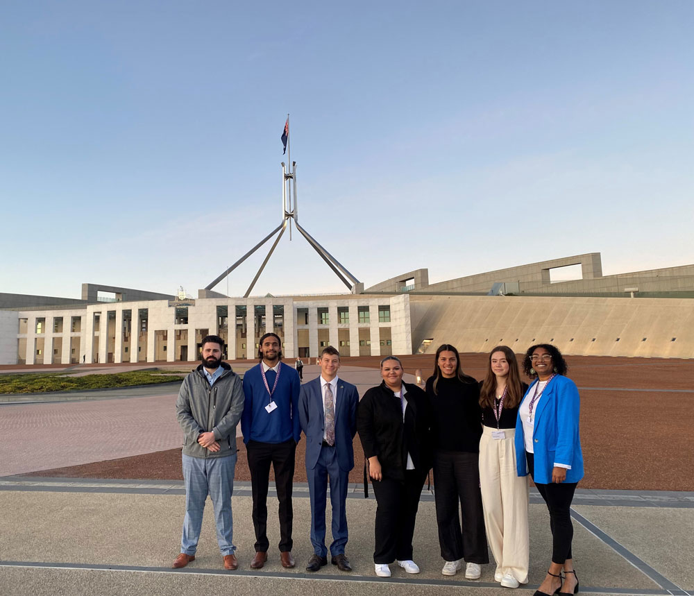 A group of first nations people standing in front of Australian parliament house
