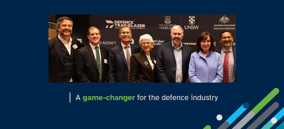 Photograph of seven people dressed in business attire and smiling at an event relating to Defence Trailblazer, with the words: A game-changer for the defence industry.