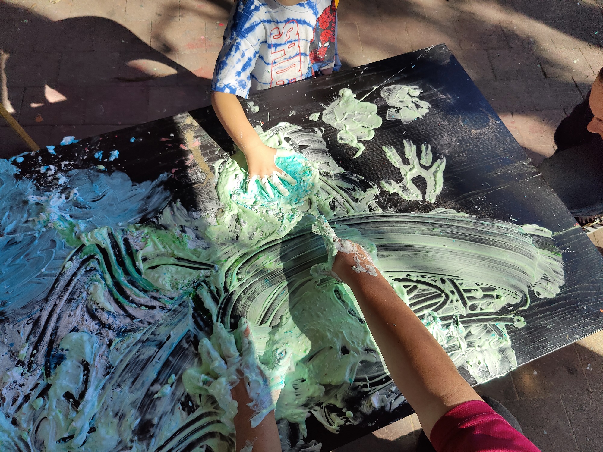 Children painting with hands on black canvas in the sunshine.