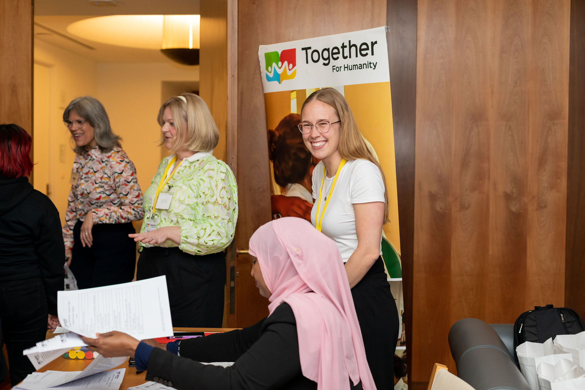 Image of 6 people in a room participating in the National Youth Summit. One woman seated at a desk and the other 5 standing and conversing.