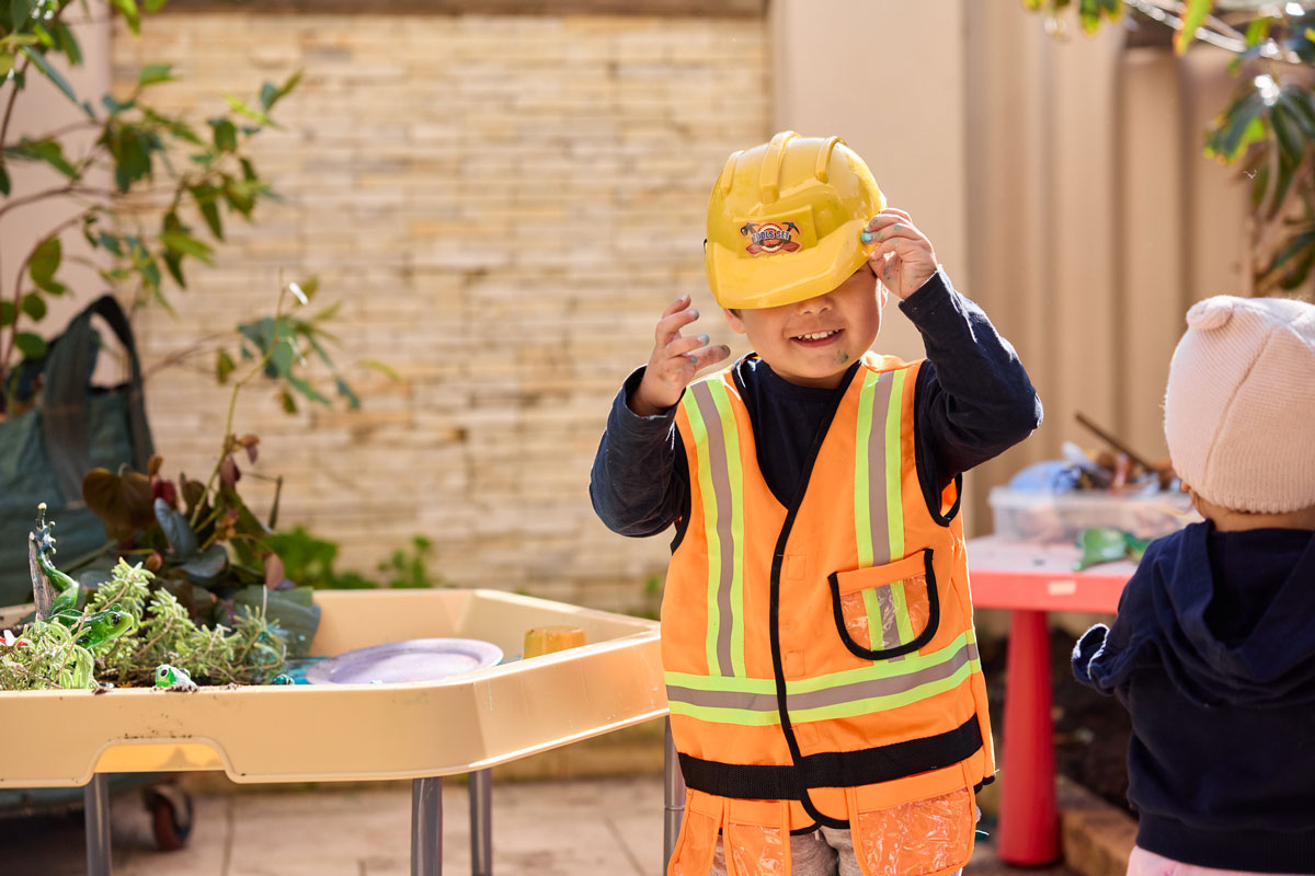 Young boy laughing wearing a construction dress up holding his hat