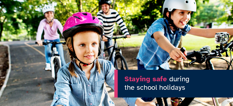 Image of 2 children and 2 adults riding bikes on a bike path with the text 'Staying safe during the school holidays'.