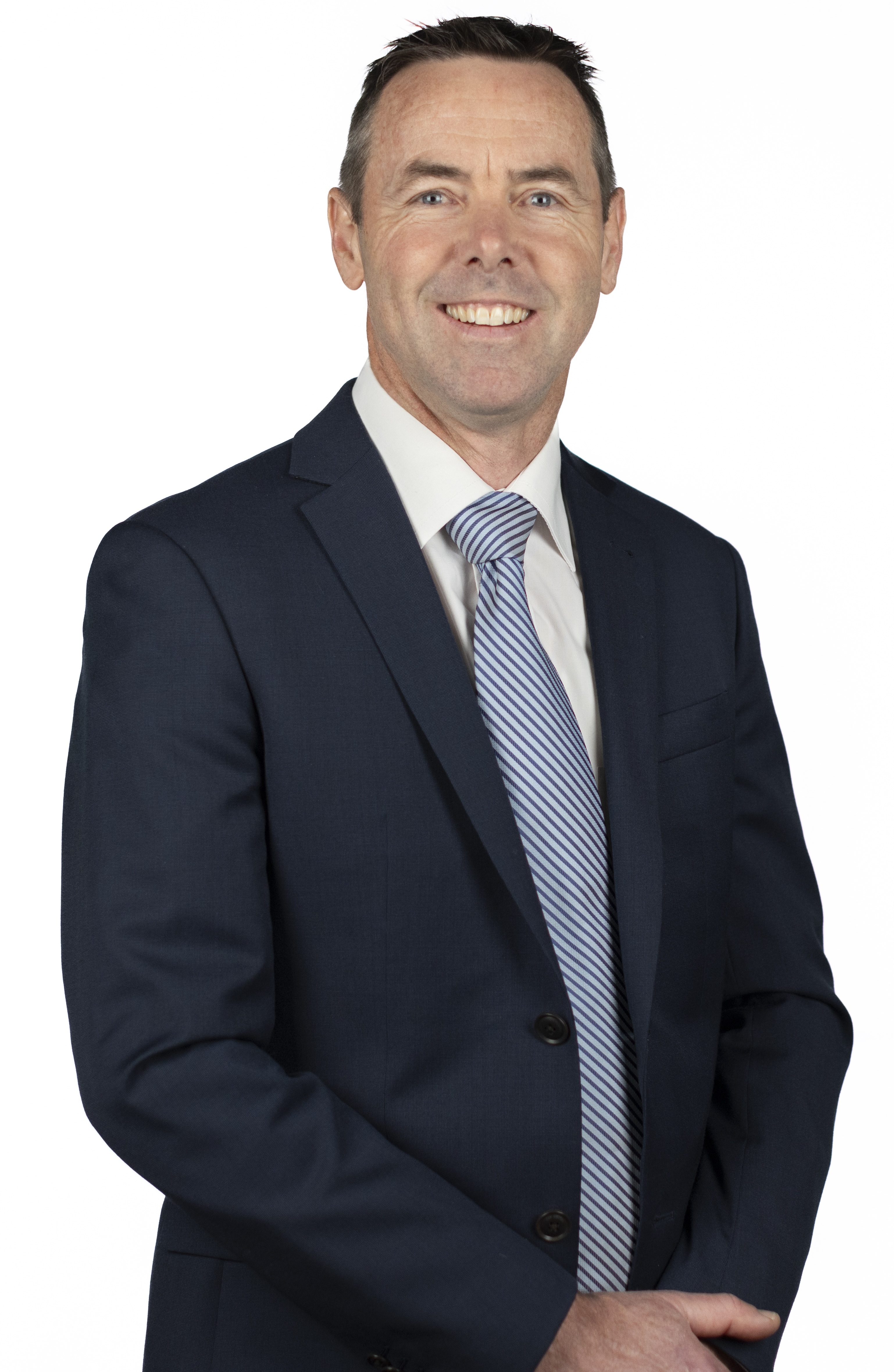 Image of Dr Peter Nolan from the waist up, slightly turned to the left smiling at the camera. Dr Nolan is in a blue suit with a white shirt and blue and white tie