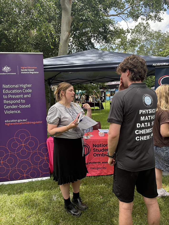 person in front of a Putting student safety first banner outside talking to another person