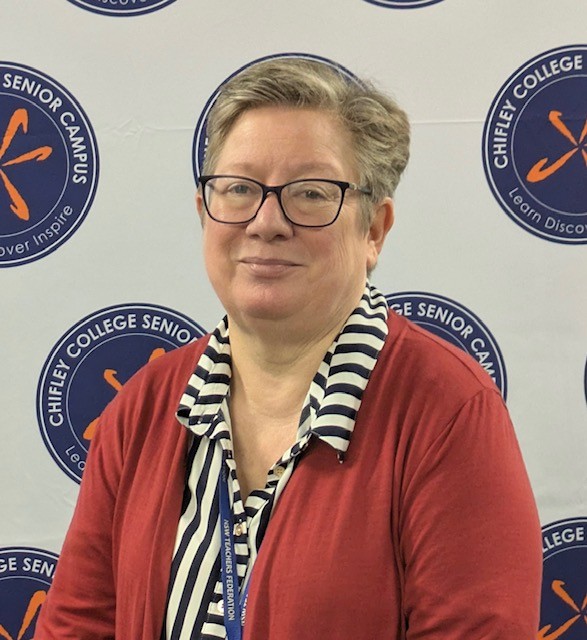 Ann Caro with short hair, wearing glasses, a stripped collared shirt and cardigan.