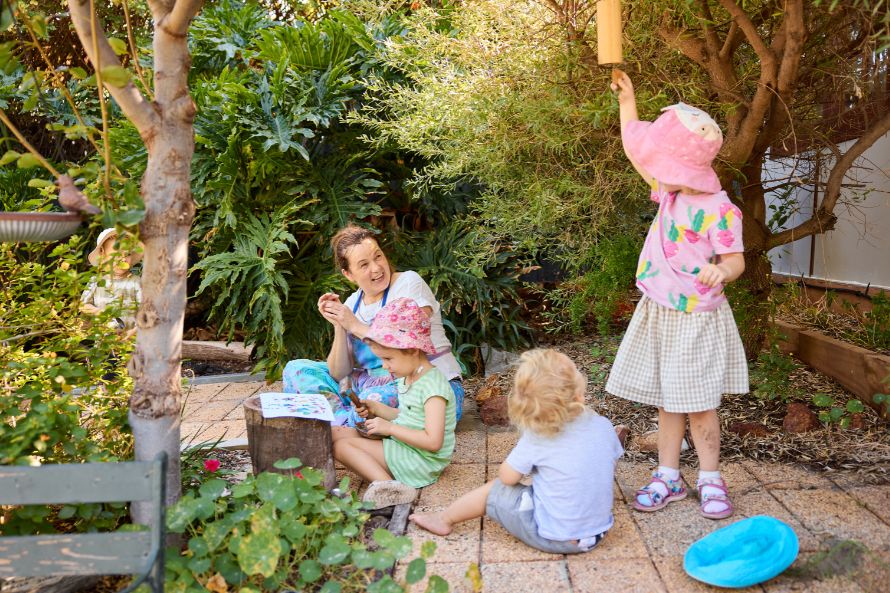 Women sitting on a garden path watching kids play nearby
