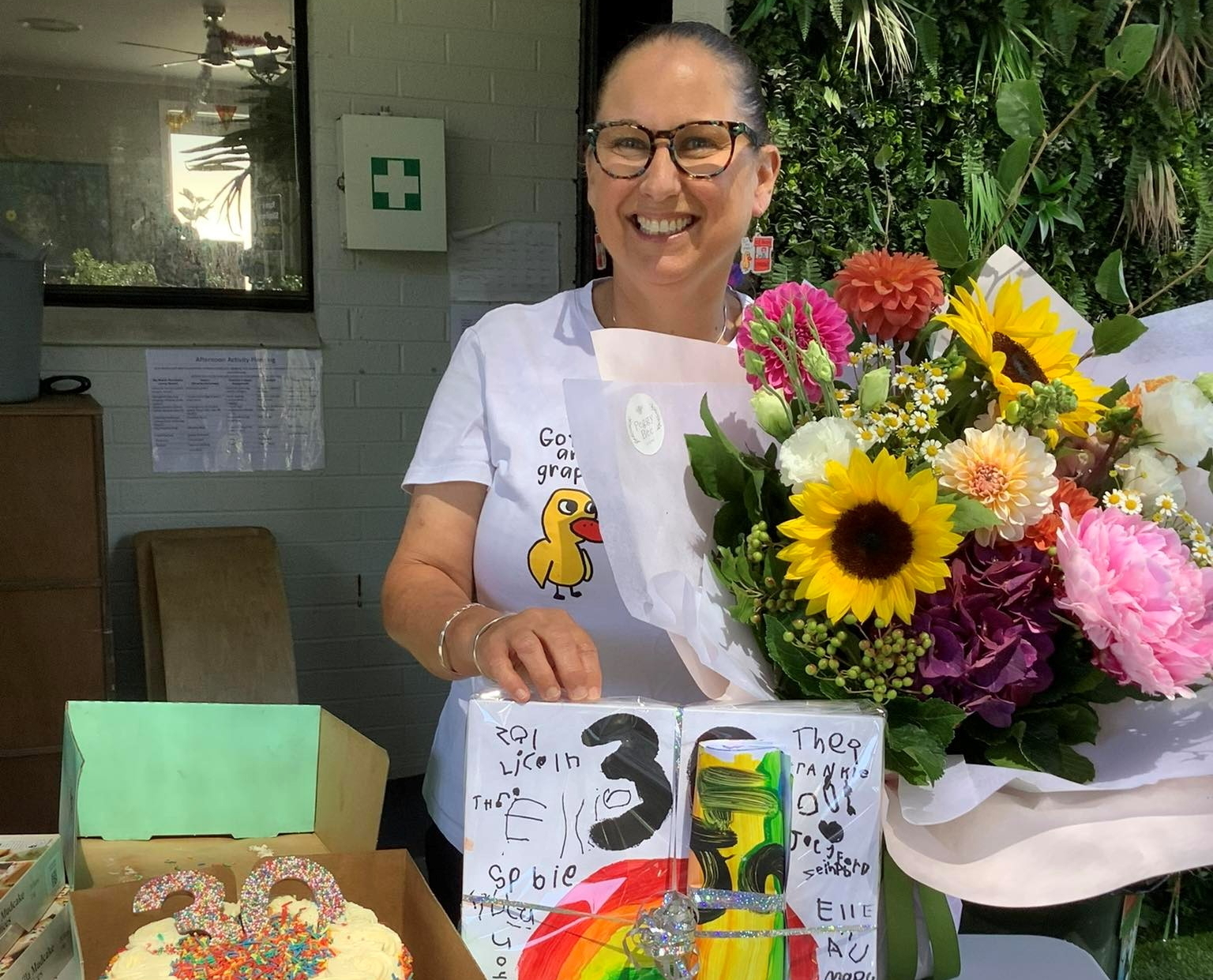 Person standing in front of birthday cake and flowers smiling
