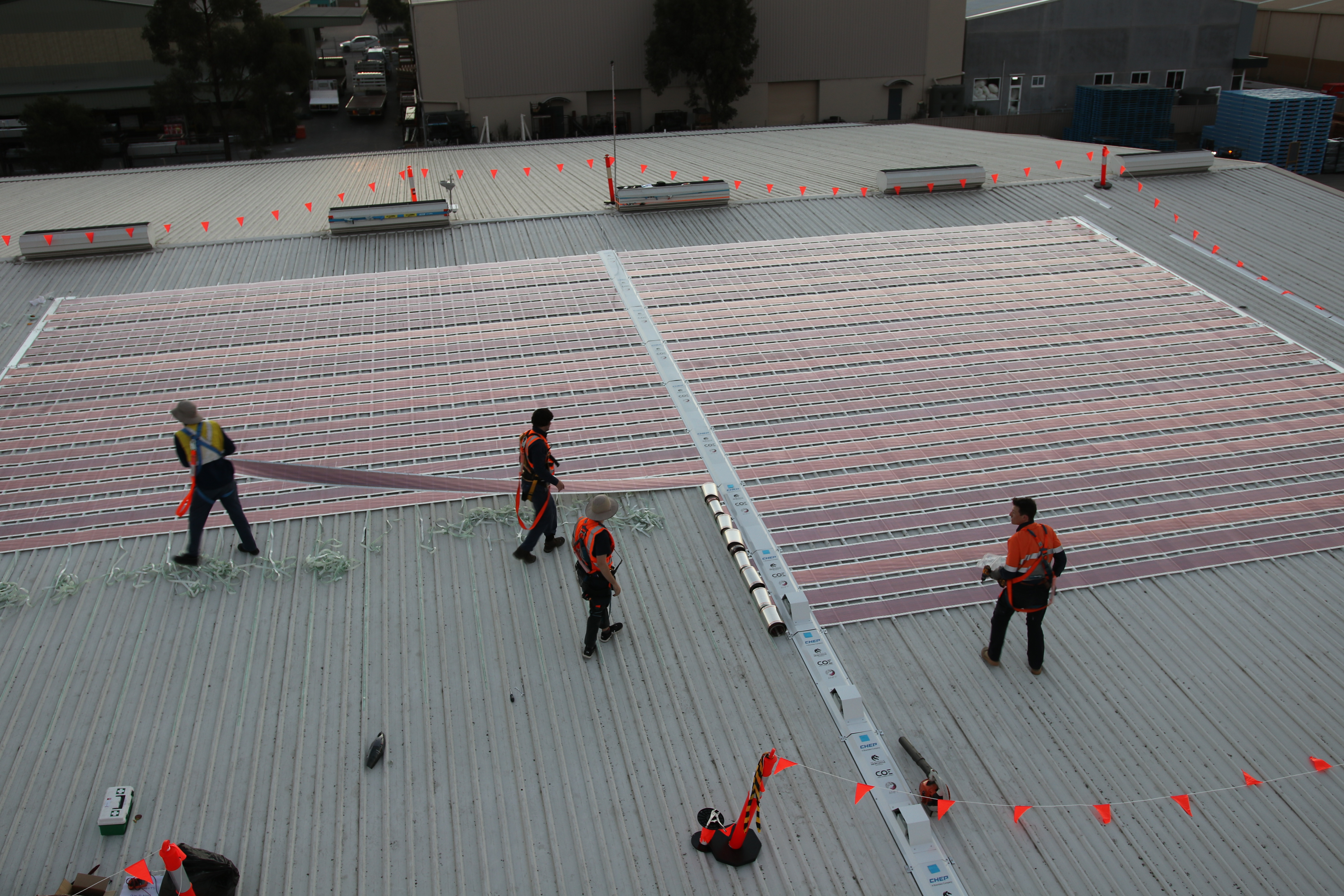Printed solar panels being installed on an industrial building rooftop.
