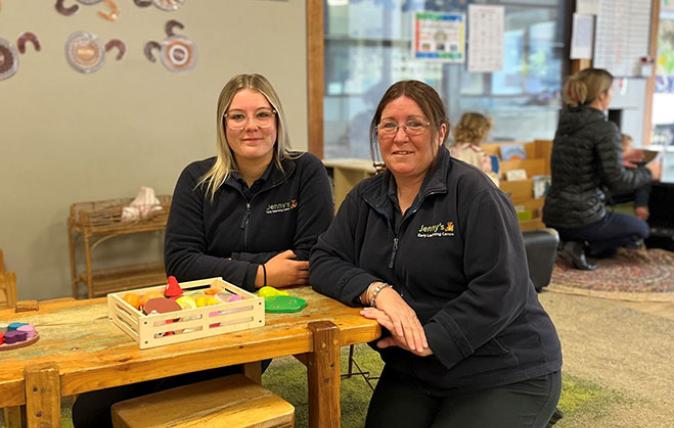 Two child care workers kneeling at a toddler table in a child care centre