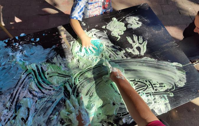 Children painting with hands on black canvas in the sunshine.