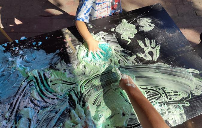 Children painting with hands on black canvas in the sunshine.