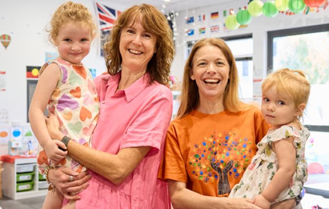 Two teachers smiling holding two young children.